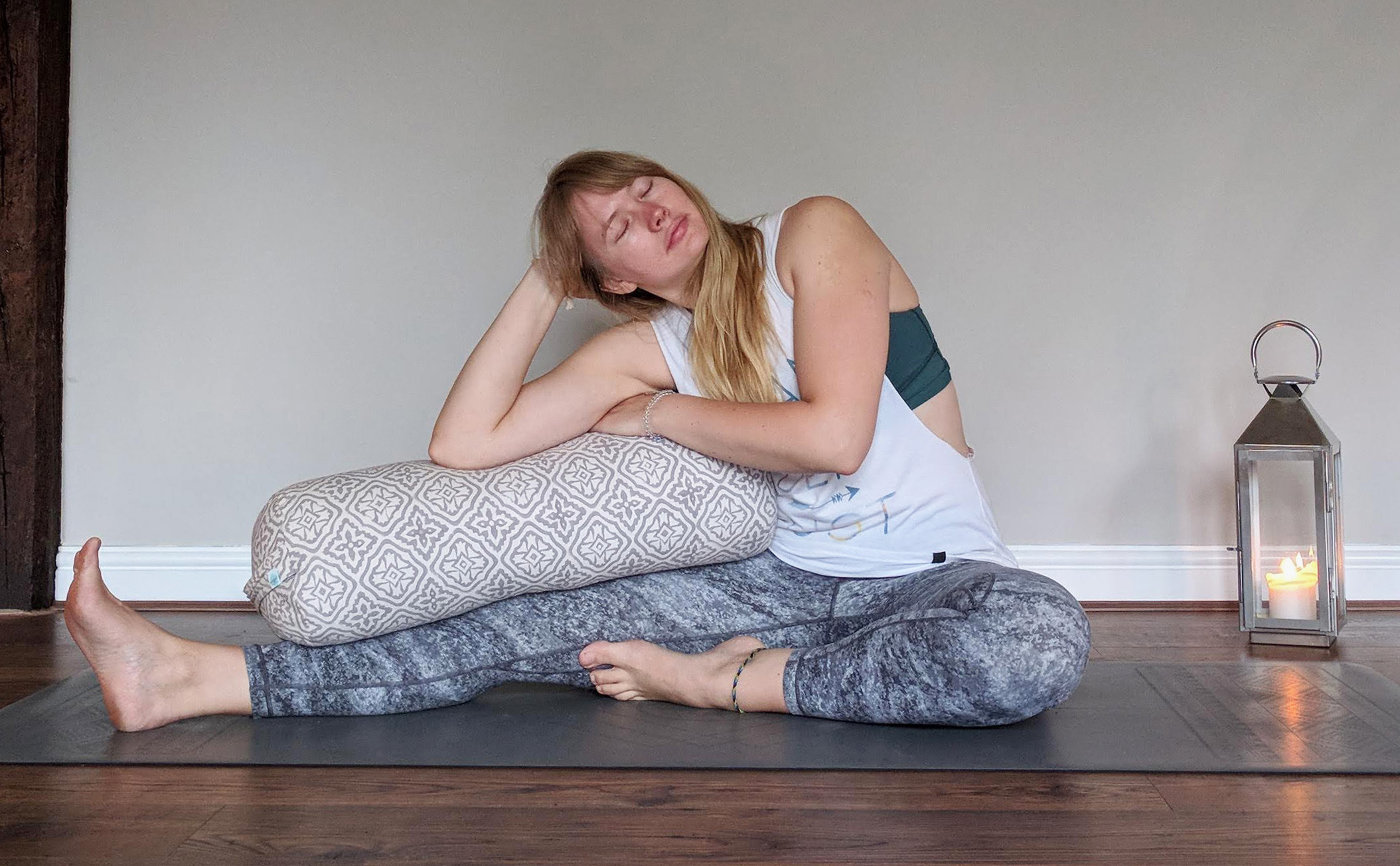 woman seated in a janu sirsasana position with bolster resting on the leg