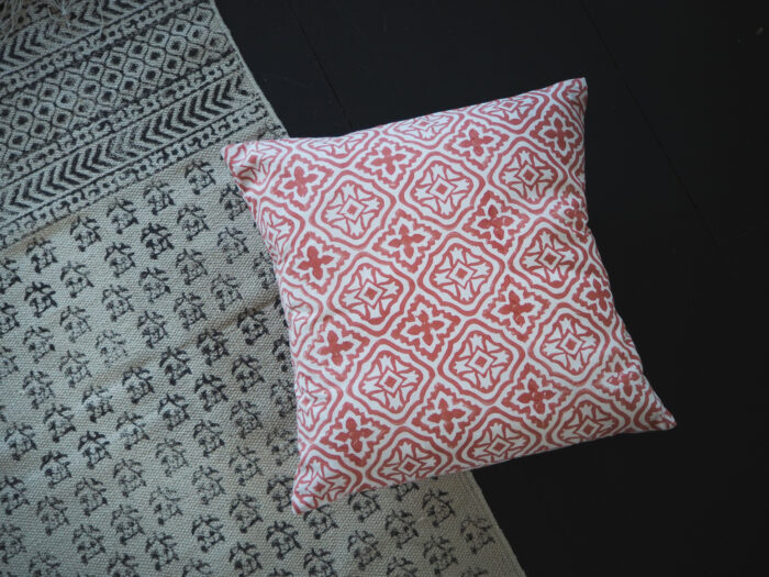 hand block printed cushion in coral pink laid on top of hand block printed rugYogipod