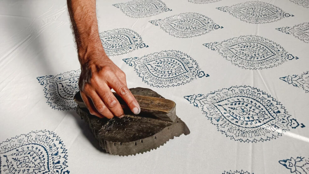 A wooden block is used to print a navy paisley motif onto white fabric for a Yogipod kantha throw