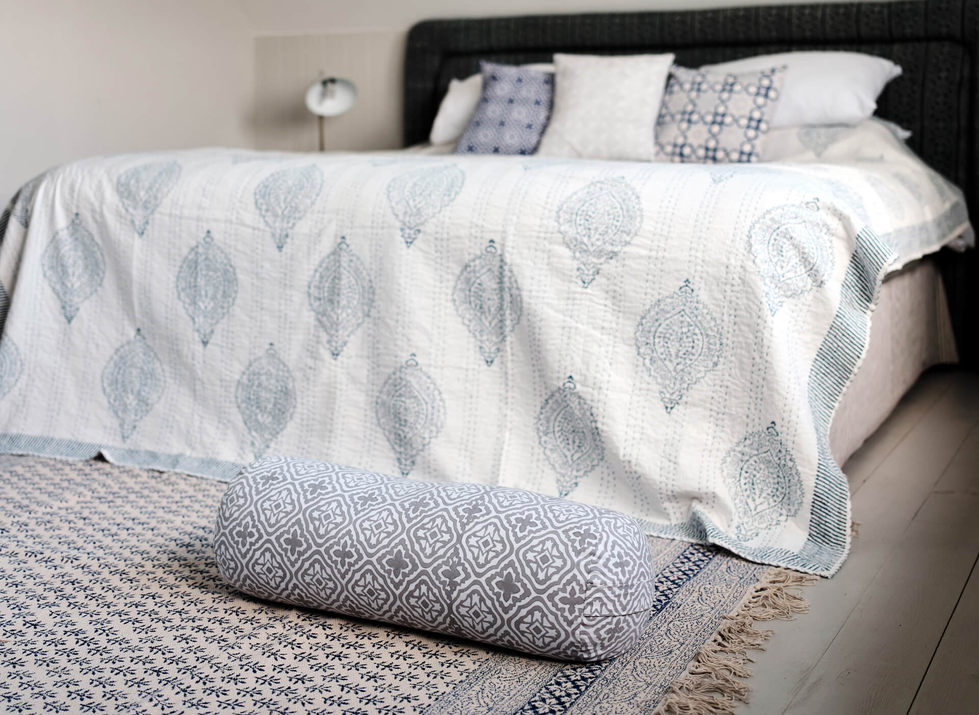 Grey Yogipod hand printed yoga bolster in a bed room infront of a bed with paisley hand printed kantha throw