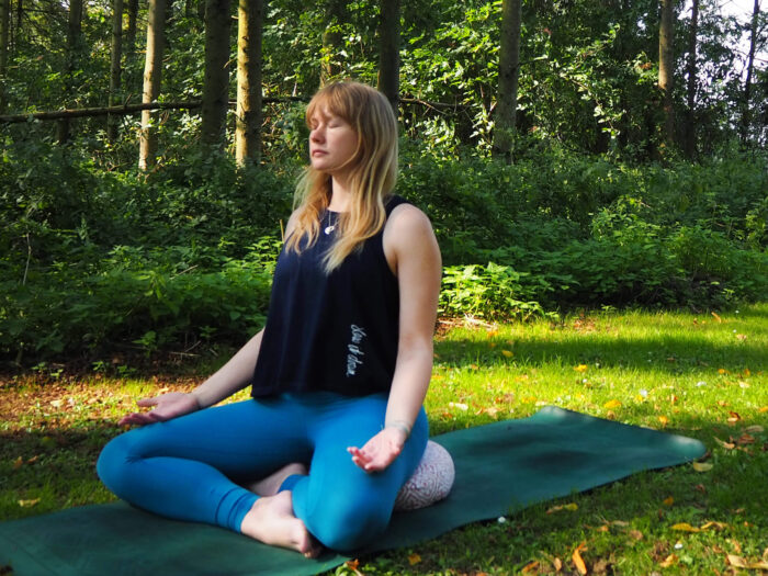 Yogipod founder Georgie sits on a meditation cushion while wearing the Slow it Down yoga vest