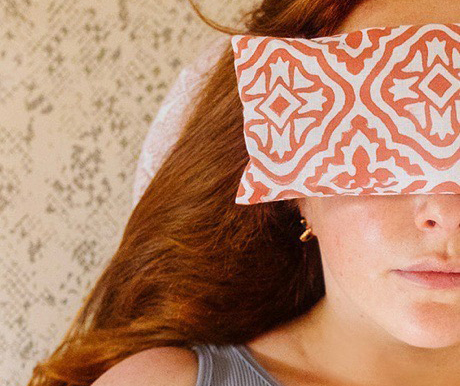 Rose lays in savasana with a pink tiled lattice print Yogipod eye pillow over her eyes